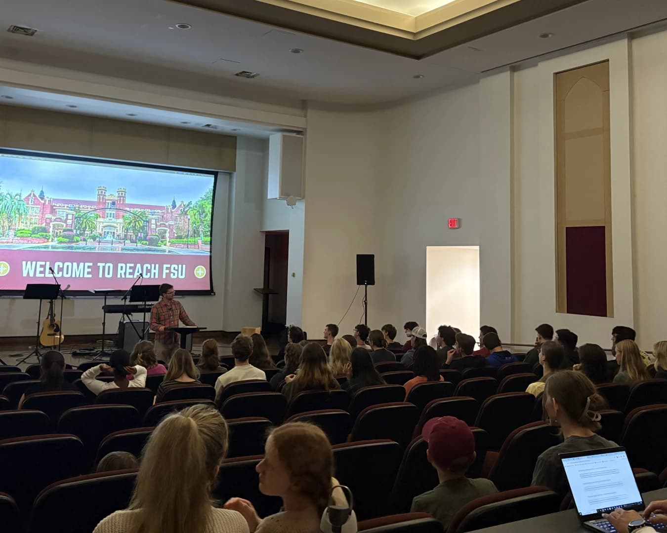 Students filling the seats of the lecture hall at Reach Night, “Welcome to Reach FSU” on the screen behind the speaker