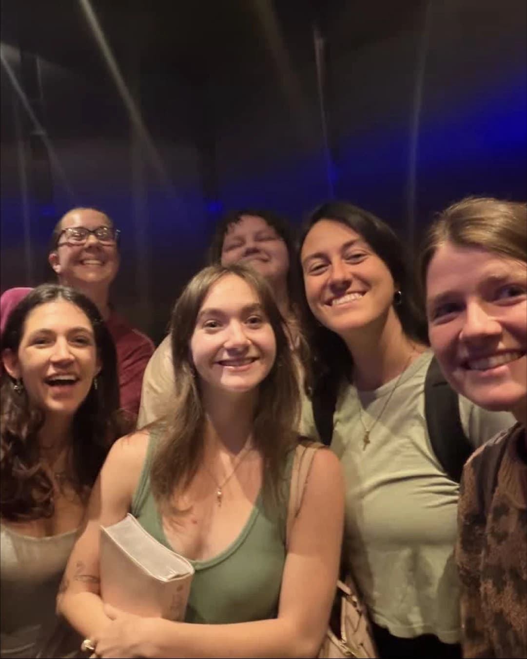 A group of students pressed together and smiling at the camera after Reach Night, one of them holding a Bible